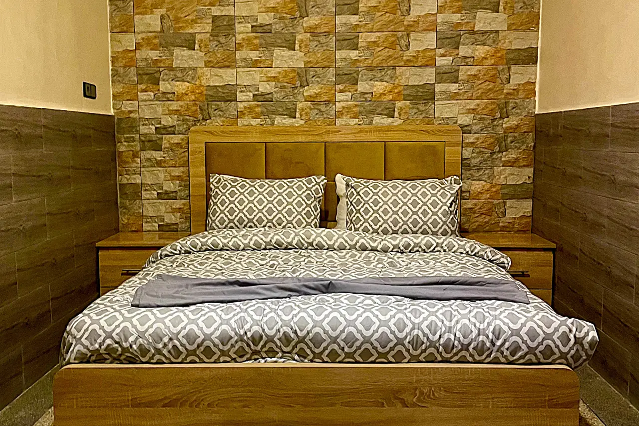 Main bedroom — centered double bed, stone accent wall and matching symmetrical bedside tables