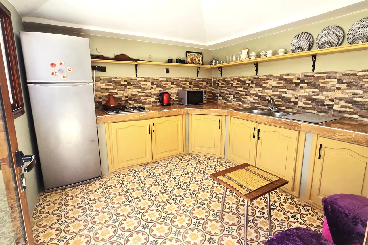 Cuisine équipée aux placards jaunes, sol en carreaux de ciment et tajine traditionnel