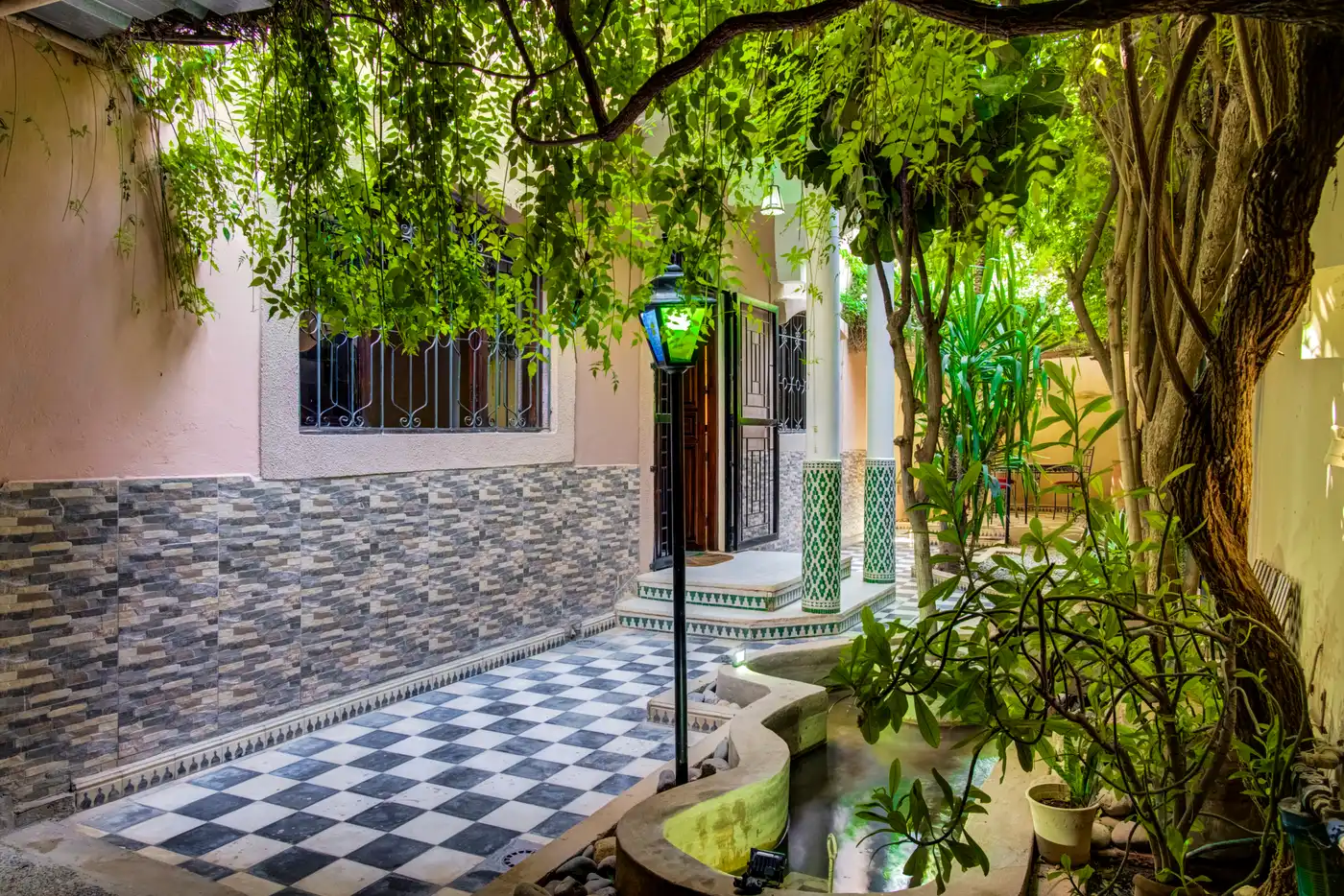 The home's garden — checkerboard walkway, green zellige columns, fountain and lush greenery