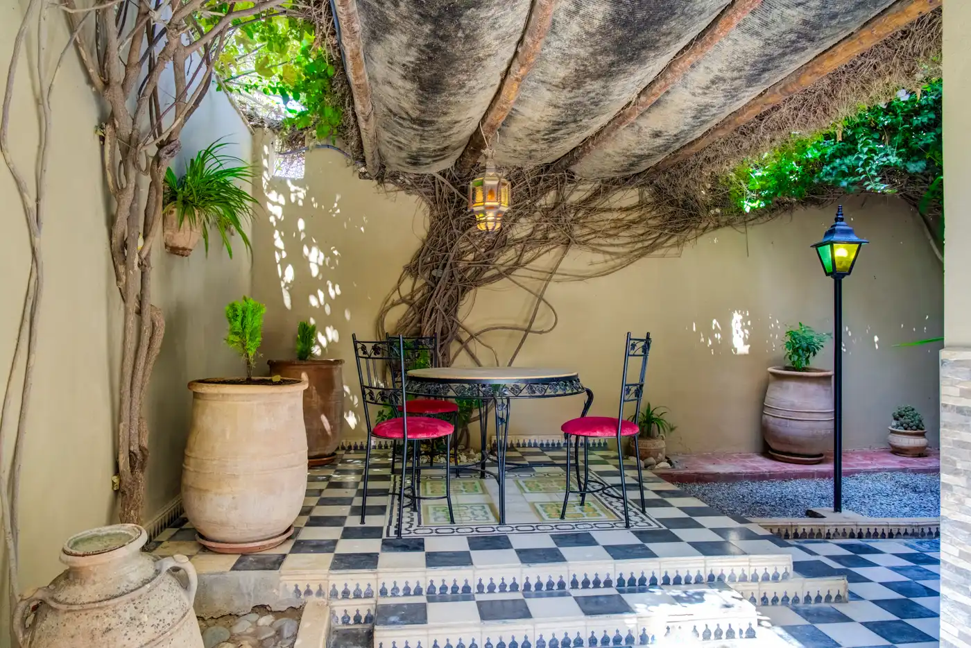 Shaded patio under the vine — wrought-iron table, pink velvet chairs and checkerboard floor