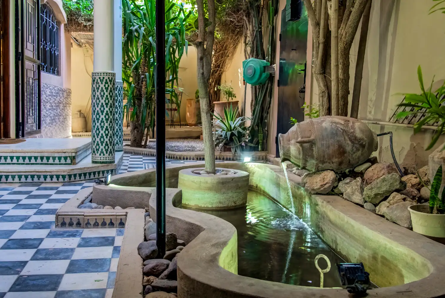 Garden fountain — terracotta amphora pouring water into a lit basin, zellige columns behind